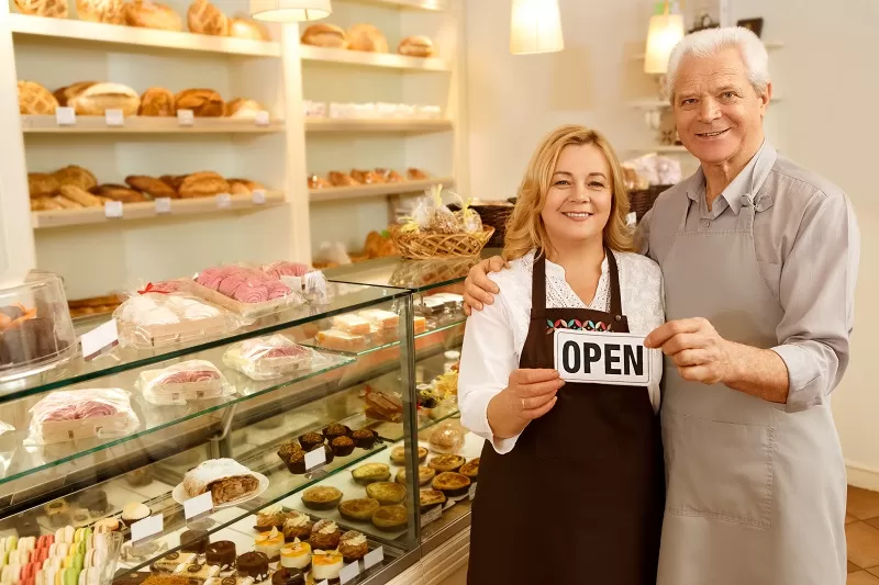 Dos personas en una panadería con el cartel de “ABIERTO”